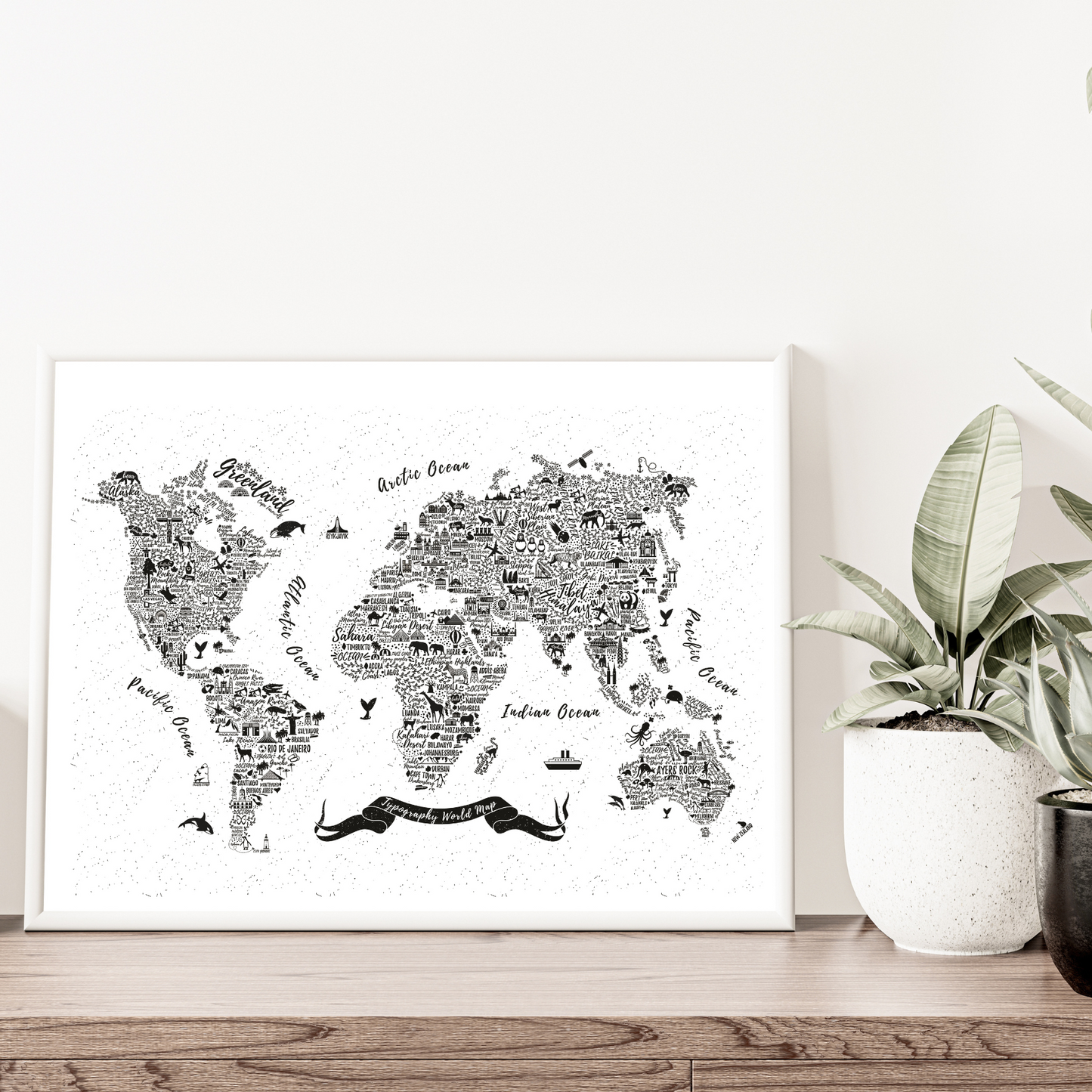 World map art print on a white wall with a plant and decorative items below.