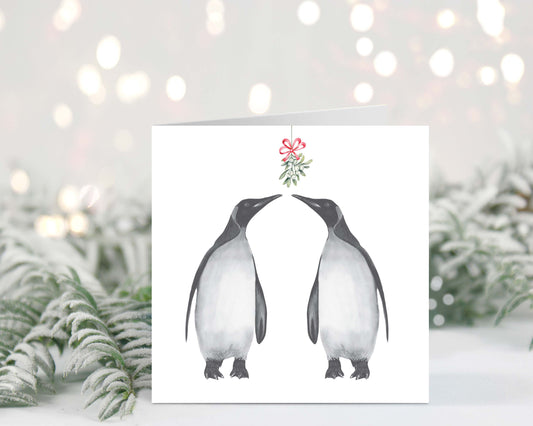 Hand-drawn penguins sharing a sweet mistletoe kiss on a festive Christmas greeting card