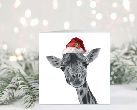 Adorable hand-illustrated Christmas card featuring Maya the giraffe wearing a festive Santa hat, perfect for sending holiday joy.