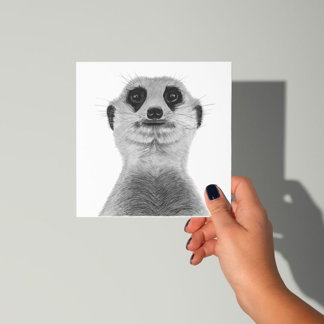 A hand-drawn Myra the Meerkat greeting card, elegantly held in hand, showcasing its charming wildlife illustration. Perfect for animal lovers and wildlife enthusiasts. Printed on Libra Fine Arts FSC-certified cardstock, offering a premium, eco-friendly choice. Blank inside, ready for a heartfelt message