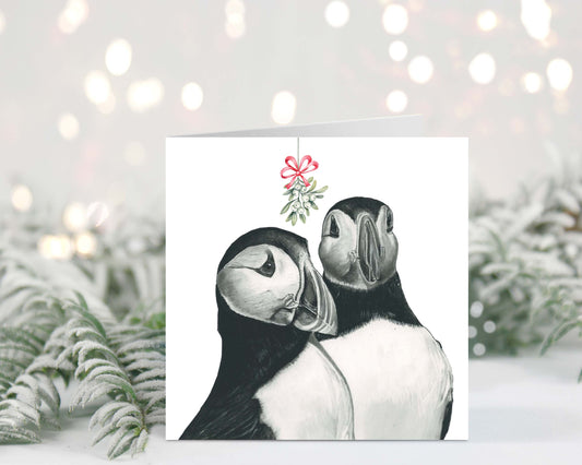 Adorable puffin couple under mistletoe, exchanging Christmas kisses on this festive holiday greeting card