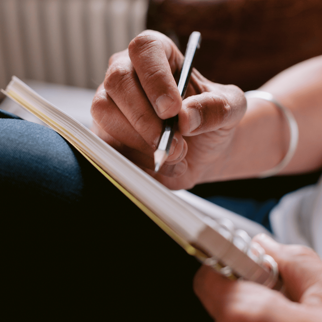 Person holding a pen and smartphone, writing in a notebook