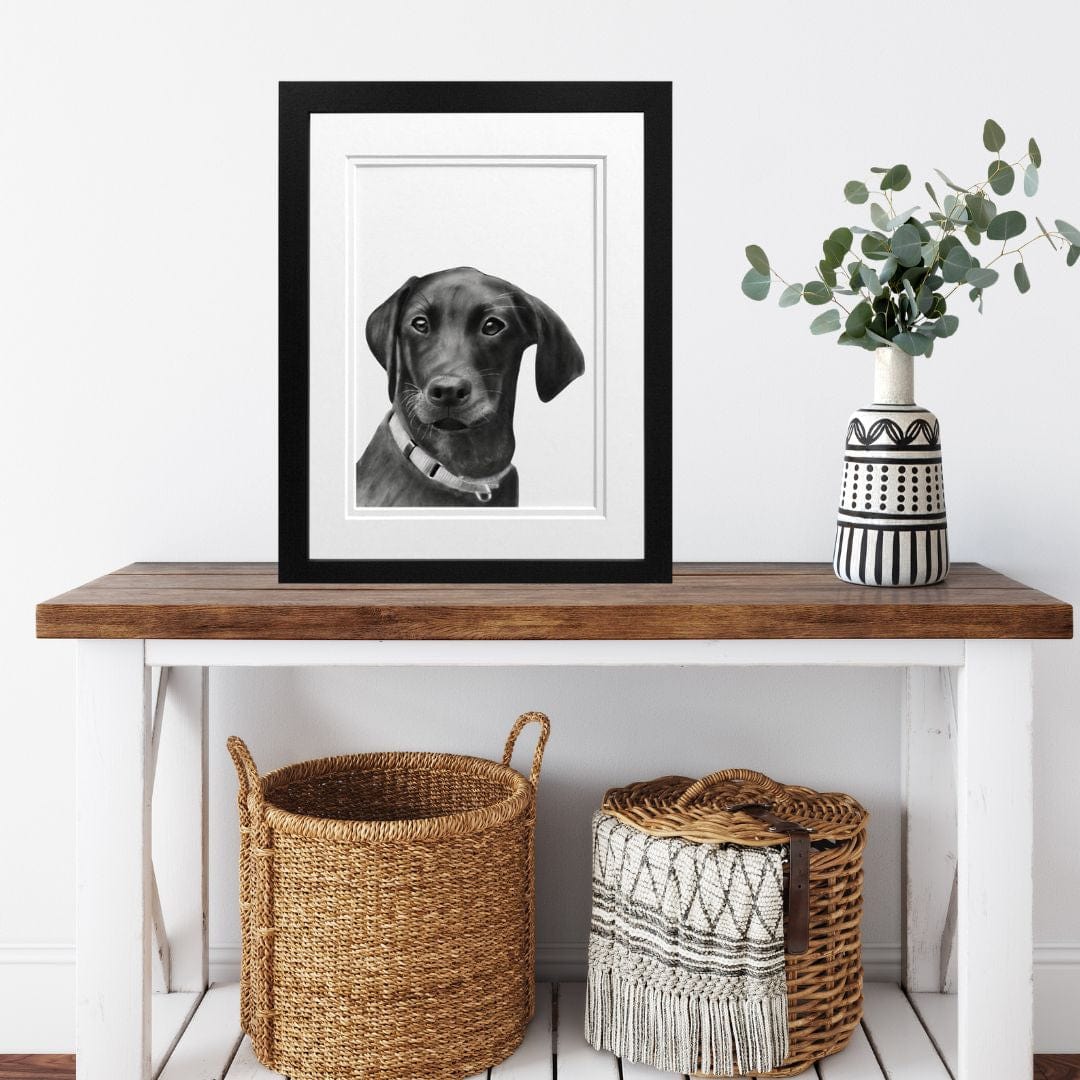 A black-framed "Labrador Dog" hand-drawn Fine Art Print by Libra Fine Arts, elegantly displayed on a sideboard with baskets neatly placed under the shelf. The bold black frame complements the detailed drawing of the Labrador, adding sophistication to the piece while the rustic baskets below enhance the natural, homely feel of the arrangement. Perfect for dog lovers, this artwork brings both warmth and style to any living room or entryway, blending seamlessly with a variety of interior styles.