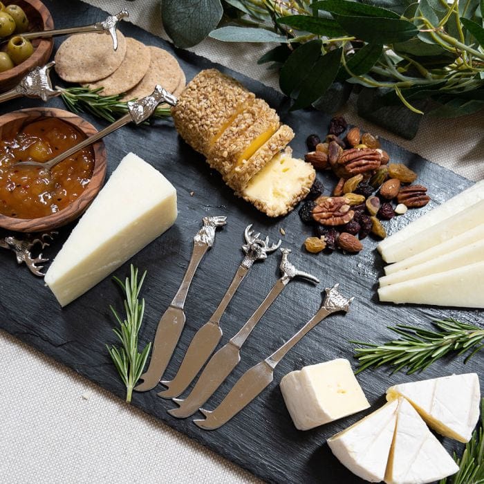 A rustic cheese platter featuring a selection of cheeses, crackers, and accompaniments, with 4 Country Animals mini cheese knives in use. Each knife is adorned with an animal design—stag, pheasant, rabbit, and Highland cow—adding a charming countryside touch to the presentation.