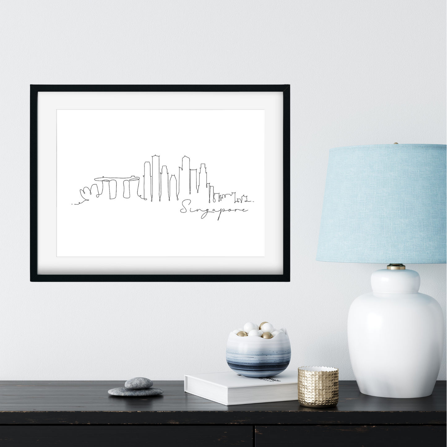 Framed artwork of Singapore skyline on a wall with decorative items below.