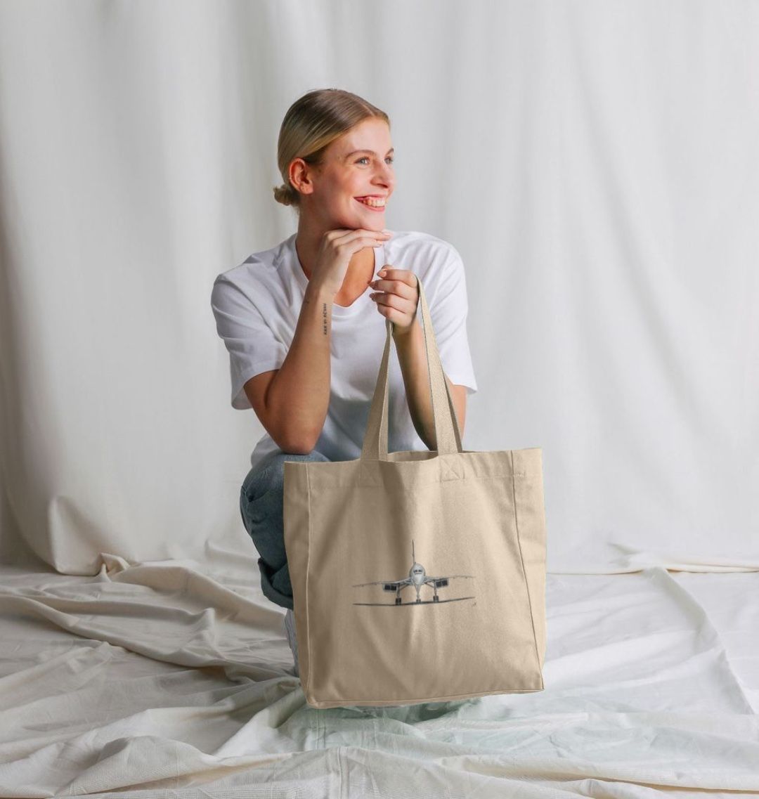 A woman carrying the Concorde Aircraft Organic Shopper Bag, crafted from eco-friendly canvas material. The bag features a detailed hand-drawn design of the iconic Concorde aircraft, showcasing both style and functionality. Perfect for everyday use, whether for shopping, errands, or carrying essentials, this durable bag is a must-have for aviation enthusiasts and eco-conscious individuals