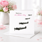 Greeting card with airplane illustrations and 'On Mother's Day' text, placed on a surface with flowers in the background.