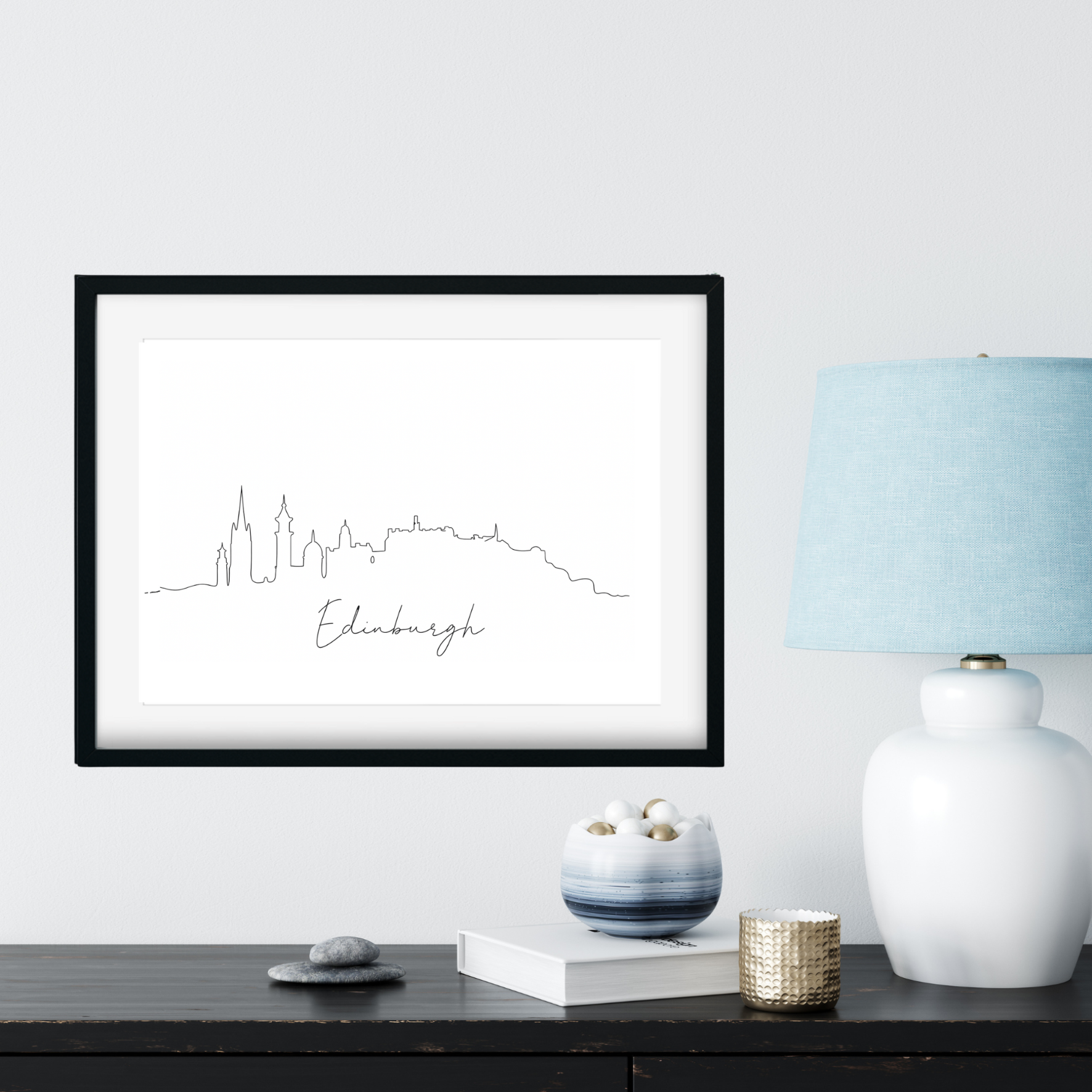 Framed artwork of Edinburgh skyline on a wall with decorative items below.