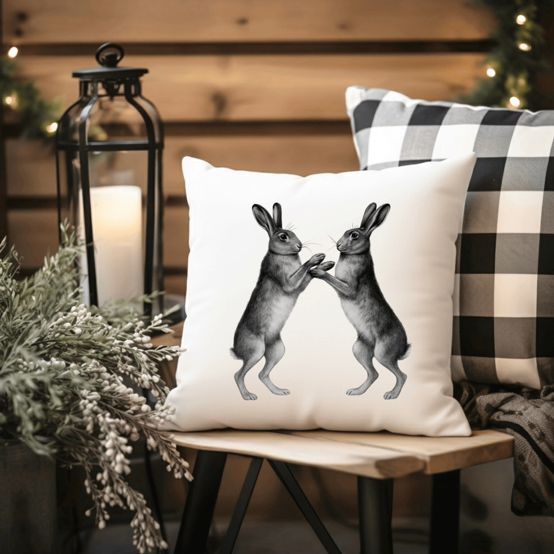 Decorative pillow with rabbit design on a wooden bench with checkered blanket and candle.