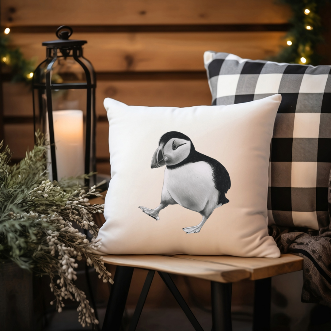Puffin-patterned pillow on a wooden stool with a candle and plaid pillow in the background