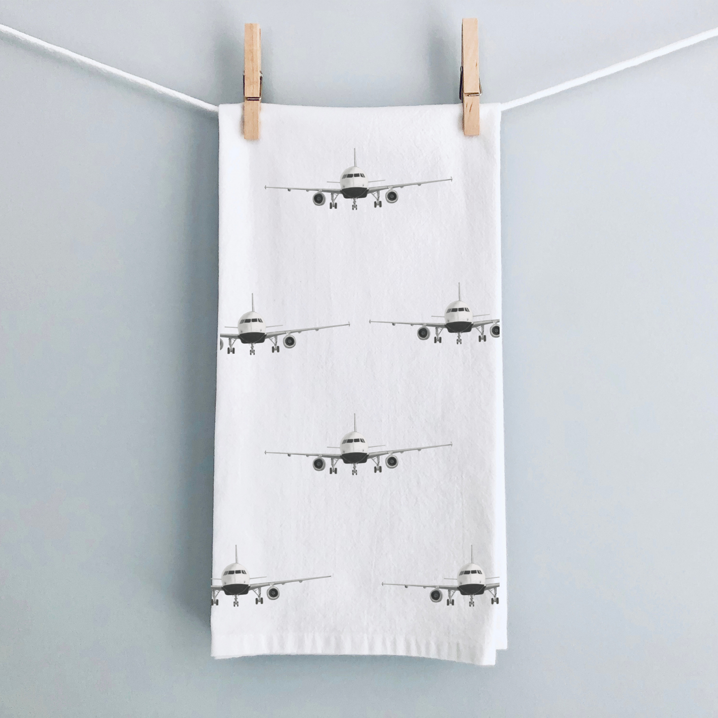 Tea towel with airplane pattern hanging on a line against a light gray background