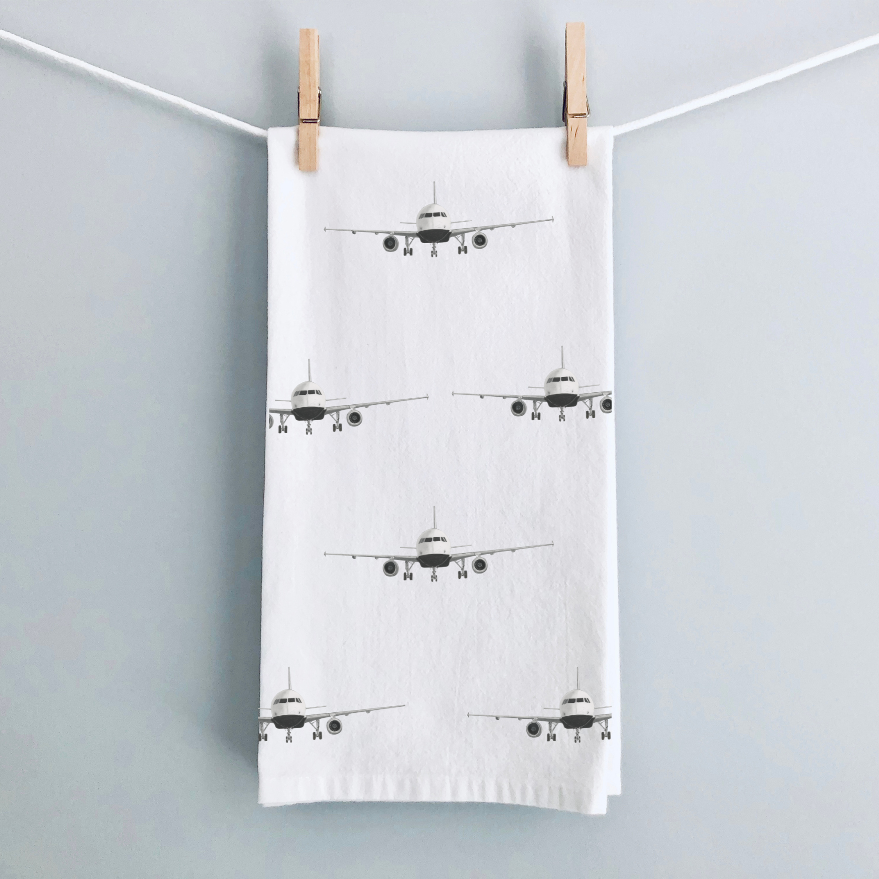 Tea towel with airplane pattern hanging on a line against a light gray background