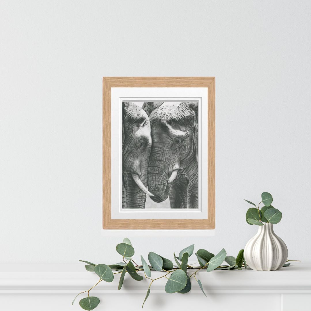 An exquisite hand-drawn fine art print of two elephants sharing a tender moment, elegantly framed in oak, ideal for wildlife enthusiasts and art collectors.