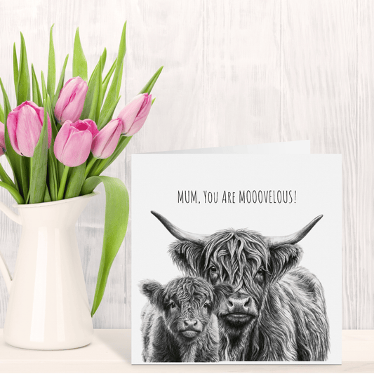 Pink tulips in a white vase next to a card with Highland cow illustration and text on a wooden surface.
