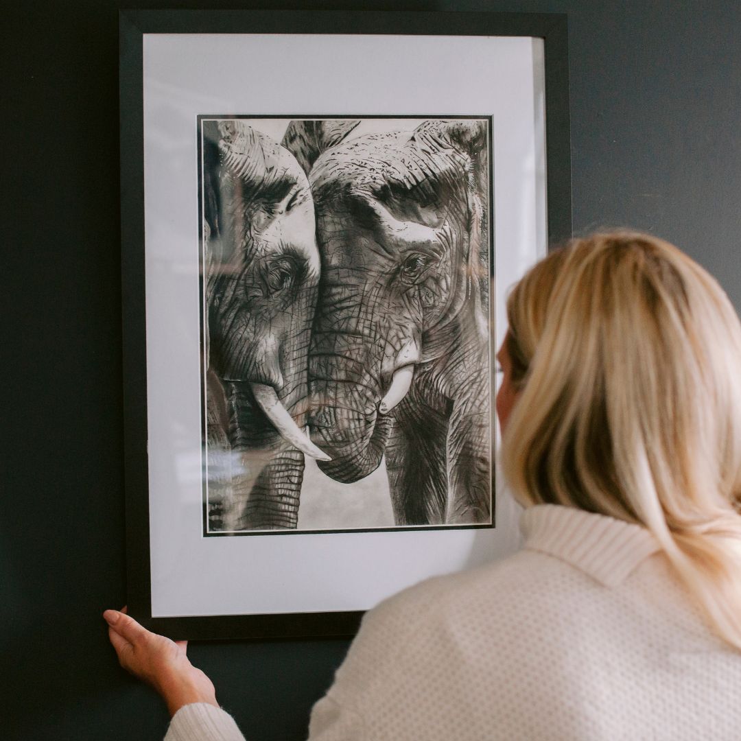 Katherine, co-founder of Libra Fine Arts, thoughtfully hanging up the hand-drawn “Elephant Tenderness” artwork in a calm, light-filled space.


