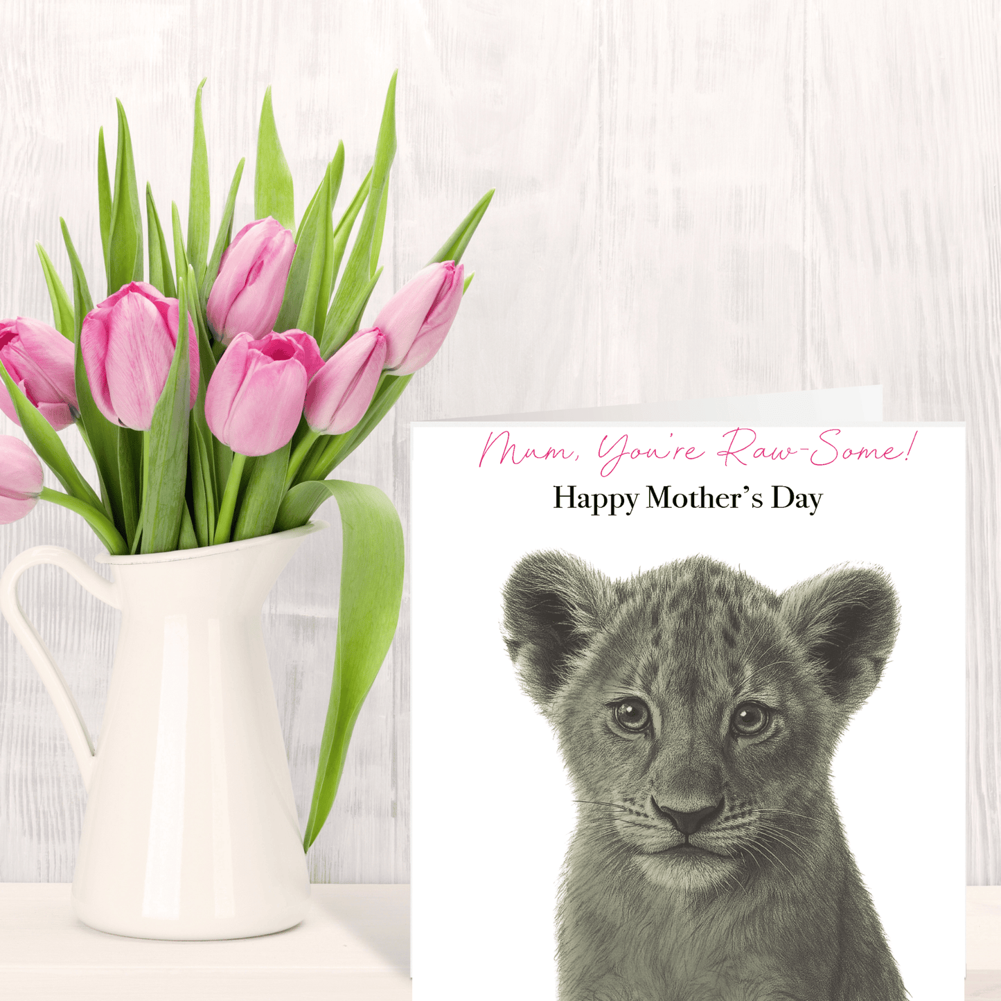 Pink tulips in a white vase next to a card with a lion cub and 'Happy Mother's Day' text on a light wooden background.
