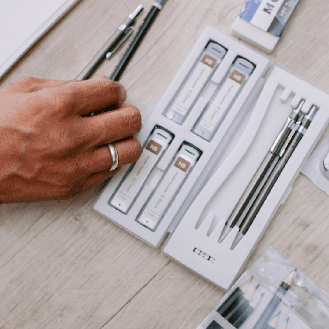 Hand holding a pen over a set of stationery items on a wooden surface
