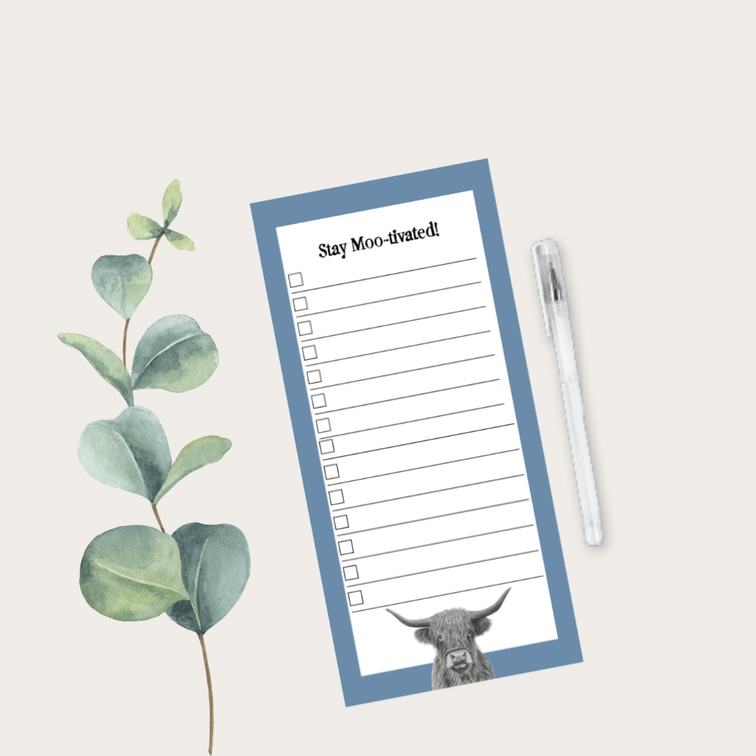 Notepad with a cow illustration and 'Stay Moo-ivated!' text on a light background with eucalyptus leaves and a pen.