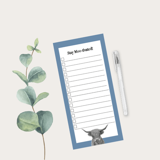 Notepad with a cow illustration and 'Stay Moo-ivated!' text on a light background with eucalyptus leaves and a pen.