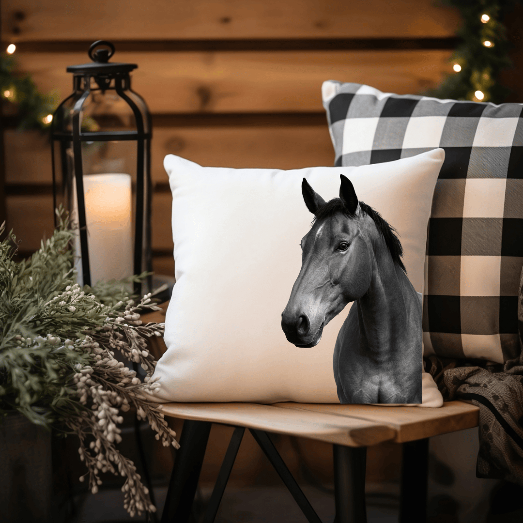 Pillow with a horse design on a wooden stool with a candle and plaid pillow in the background.