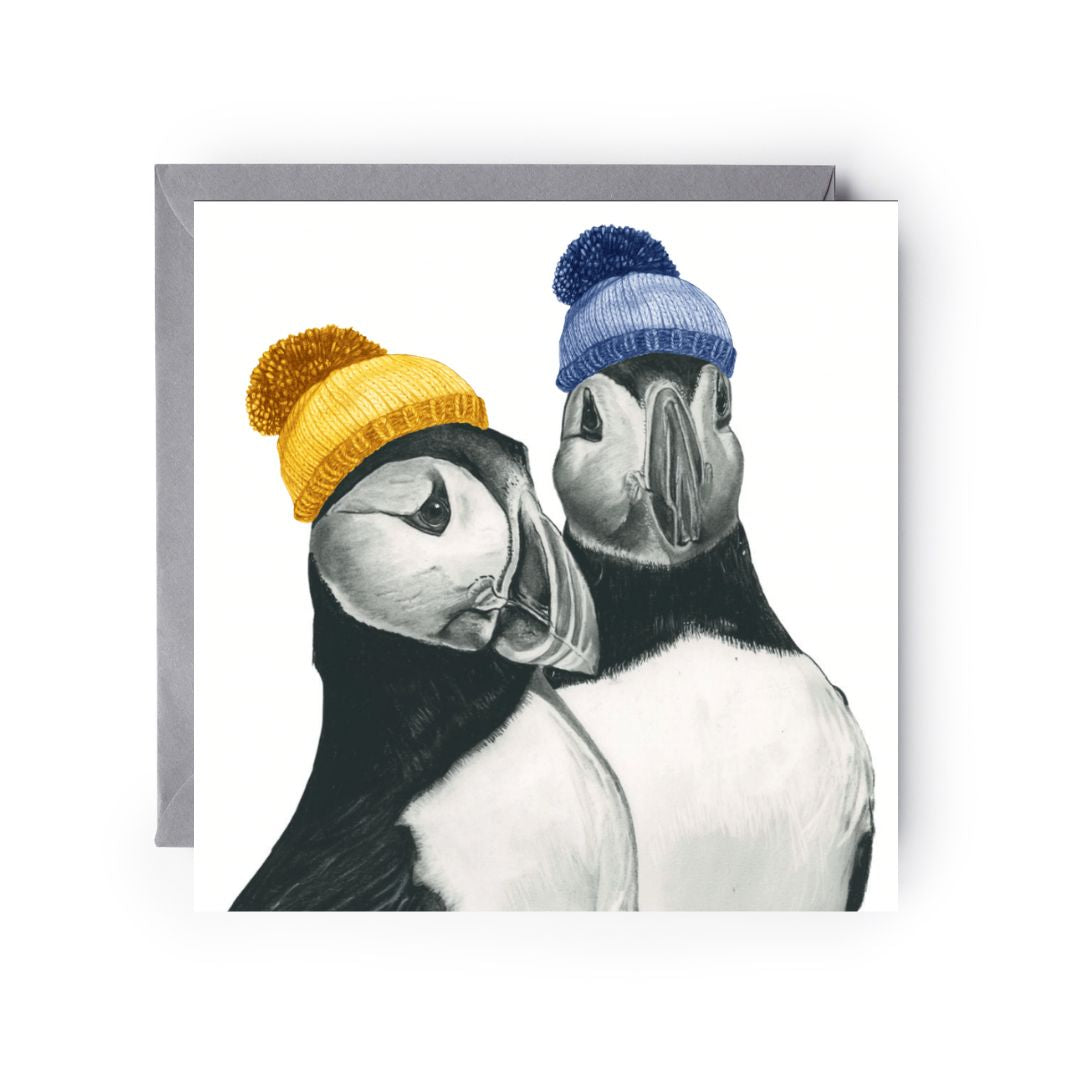 Hand-drawn winter greeting card featuring a pair of puffins in a coastal winter scene.

