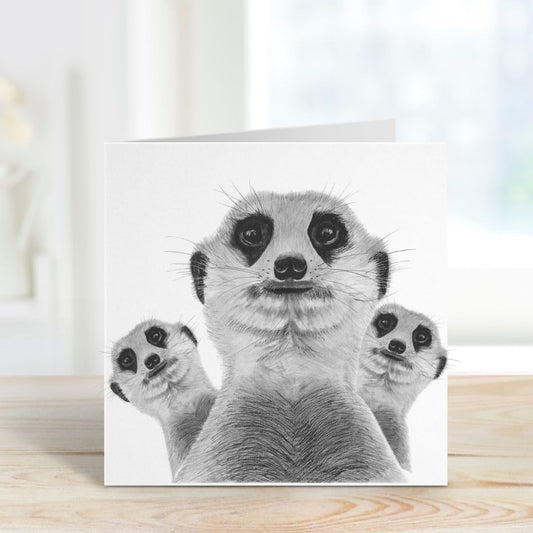 The Meerkat Madness Greeting Card is open, showcasing the vibrant hand-drawn image of a fun-loving meerkat family. Their playful antics are sure to bring a smile, with the charming card standing tall to display the artwork.