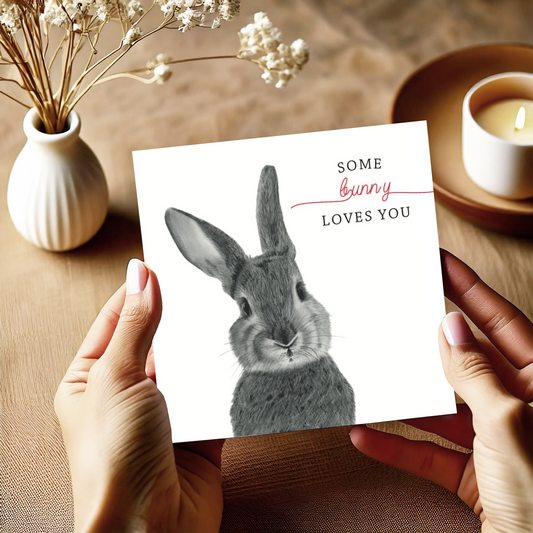 A hand-drawn "Some Bunny Loves You" greeting card, featuring an adorable bunny design, held in a woman's hands. The card is accompanied by a red envelope, making it perfect for anniversaries, birthdays, or to show someone special how much you care. Printed on high-quality cardstock, the card is blank inside, ready for a personal message. Ideal for animal lovers and anyone who appreciates charming, thoughtful cards.








