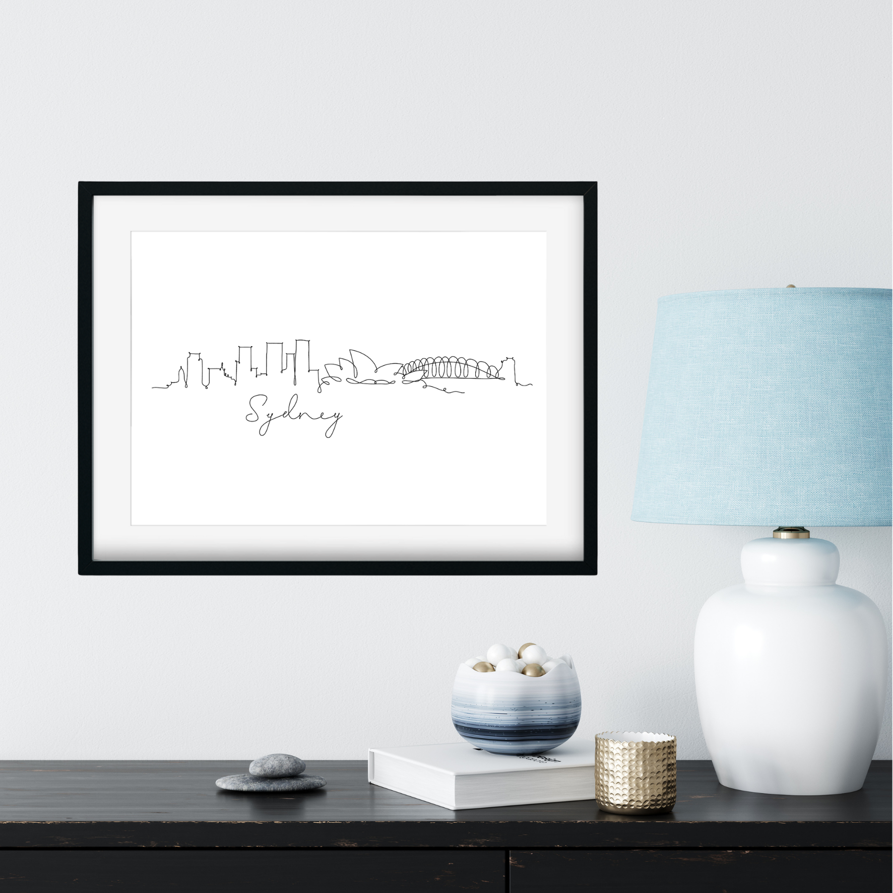 Framed artwork of a city skyline with 'Sydney' text, placed on a shelf with decorative items.